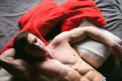 High angle view of shirtless muscular male model lying on bed at home