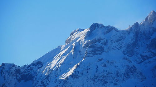 Low angle view of snowcapped mountains against clear blue sky