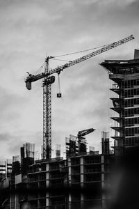 Low angle view of cranes at construction site against sky in city