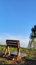 Empty bench on field against clear blue sky