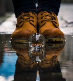 Low section of person reflecting on crystal ball at puddle