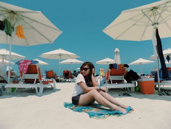 Young woman sitting on towel by parasols at beach