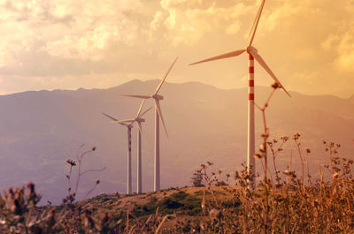 Scenic view of landscape and wind turbines against mountain and  cloudy sky