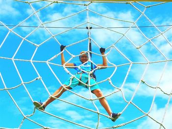 Low angle view of young woman climbing ropes at playground against sky