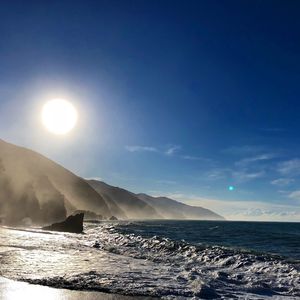 Scenic view of sea and mountains against bright sun