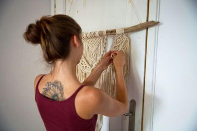 Rear view of woman standing against wall at home