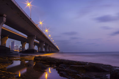 Illuminated bridge over sea against sky at sunset