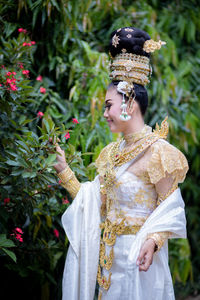 Bride wearing wedding dress with jewelry while standing by plants