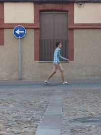 Young man walking on footpath by building