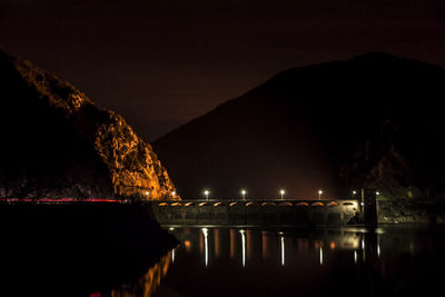 Illuminated bridge over river against sky at night