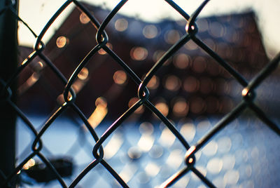 Close-up of chainlink fence against buildings during winter