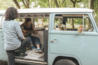 Rear view of man looking at female friend playing guitar inside van