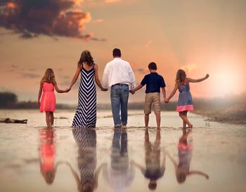 Family walking at beach against sky during sunset