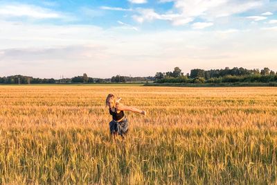 Woman with arms raised on field against sky