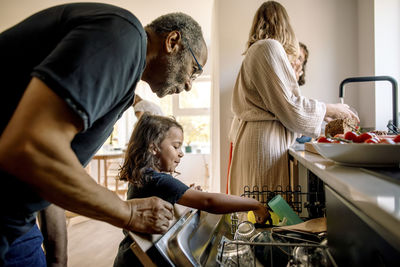 Grandfather assisting grandson loading utensils in dishwasher at home