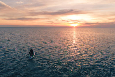 A silhouette of a man surfing with a paddle in open sea  into the sun