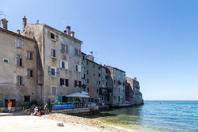 Buildings by sea against clear blue sky