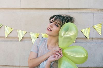 Young woman holding balloons against wall