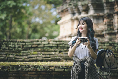 Young woman photographing with mobile phone standing outdoors