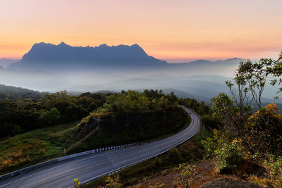 Road amidst trees against sky during sunset