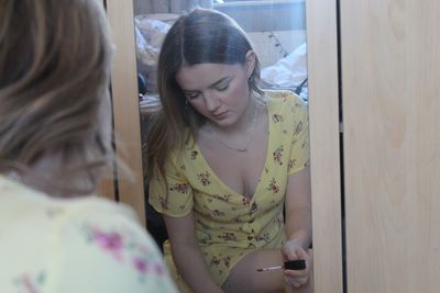 Beautiful woman applying nail polish reflecting in mirror