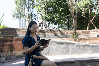 Full length of young woman using phone while sitting on tree