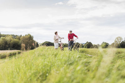 Senior couple pushing bicycles in rural landscape