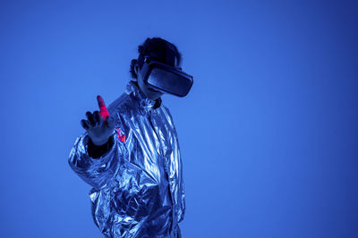 Woman wearing virtual reality simulator gesturing by standing against blue background