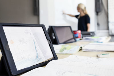 Close-up of digital tablet on desk with teacher explaining in background