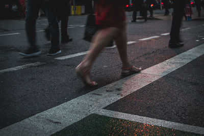 Low section of woman walking on road in city