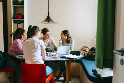 Female friends discussing while studying together at home