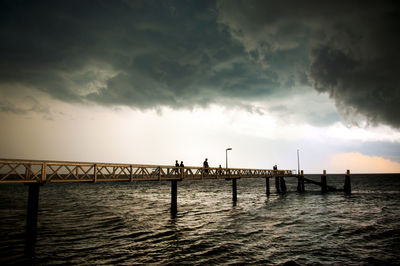 Huge black storm clouds gather as silhouetted people fish off a pier