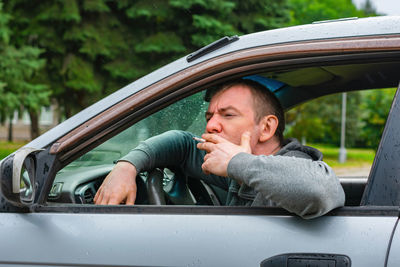 The driver smokes a cigarette in the car in the rain