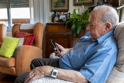 Elderly man using a mobile phone and wearing a smart emergency alarm bracelet around wrist at home