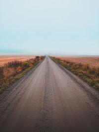 Dirt road amidst landscape against sky