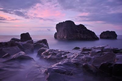 Rocks in sea against sky during sunset