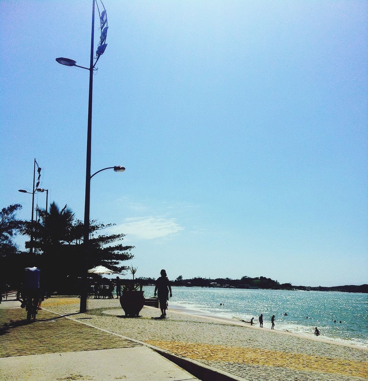 clear sky, water, sea, copy space, transportation, beach, tree, blue, tranquility, mode of transport, tranquil scene, nature, shore, bicycle, incidental people, scenics, street light, nautical vessel, horizon over water, sand