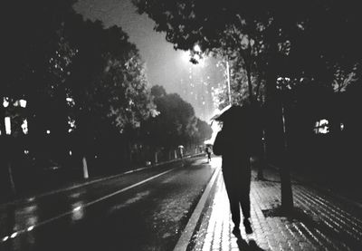 Rear view of silhouette woman walking on wet road during rainy season