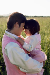 Korean man with a daughter child stands on a green field at sunset in summer in national costumes