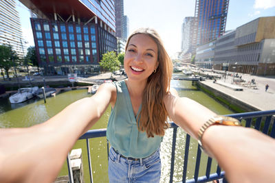 Beautiful young woman taking self portrait with rotterdam cityscape on the background, netherlands