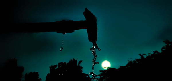 Silhouette of water drops on metallic structure against sky at sunset