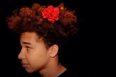 Close-up of boy with flower in hair against black background