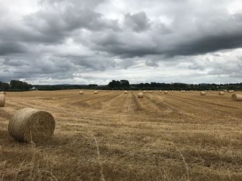 Hay bales on field against cloudy sky