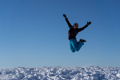 Woman jumping on snow covered land against blue sky