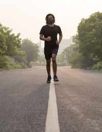 Front view of a man wearing a mask while running on an empty road during sunrise.