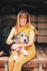 Smiling woman holding dog while sitting outdoors