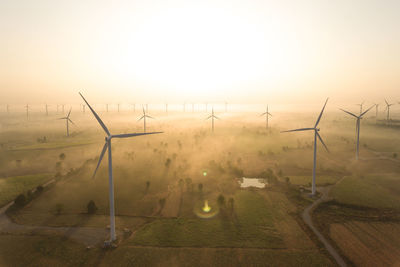 Wind turbines on field against sky during sunset