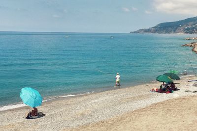 People sitting on beach by sea against sky