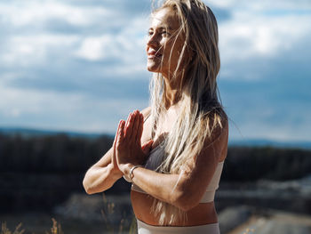 Young beautiful blond woman with long hair in activewear sitting in a lotus pose in a hill