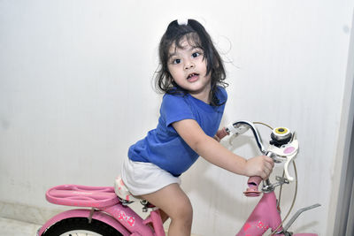 Portrait of cute girl sitting on bicycle against wall